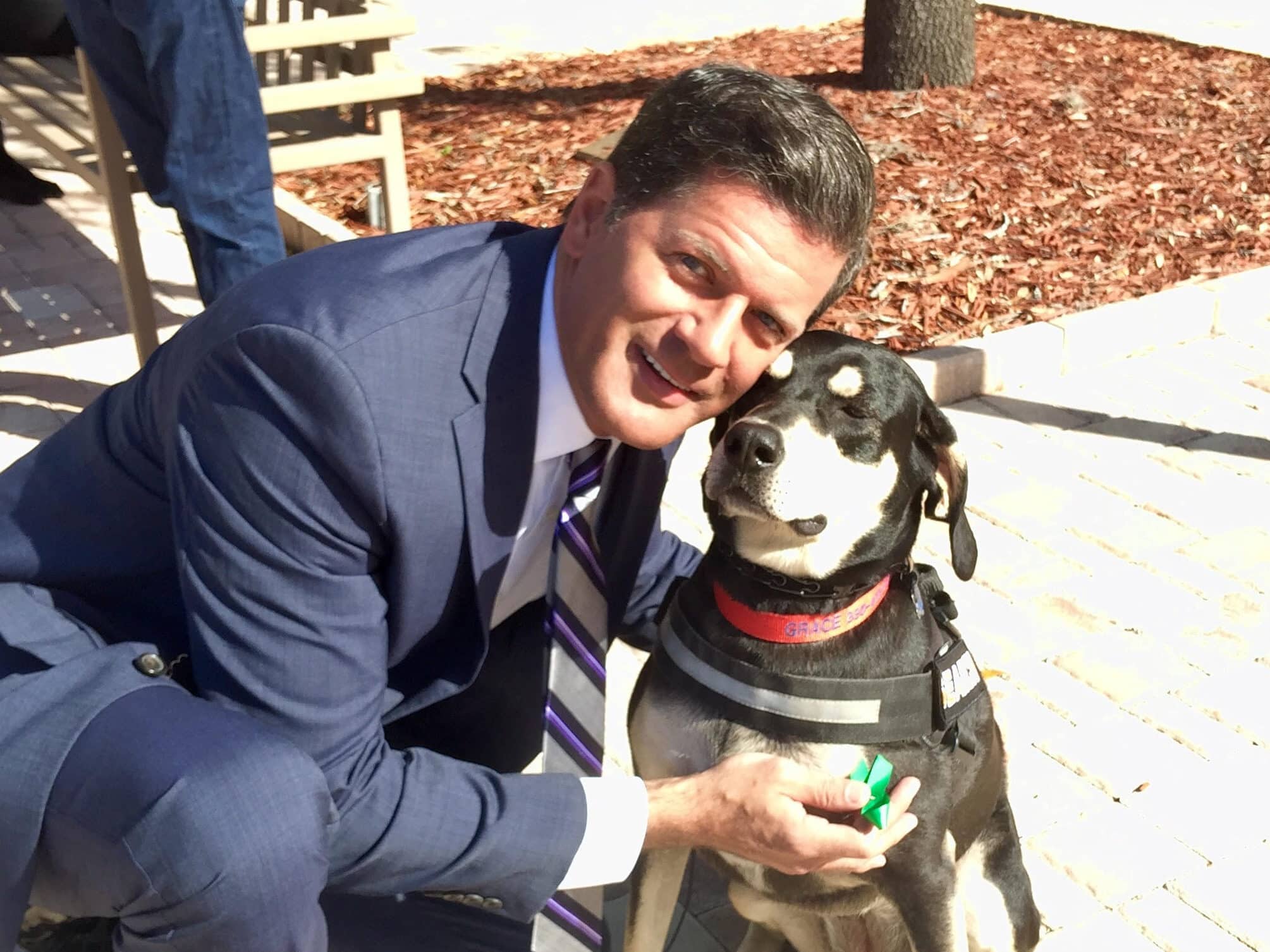 Man in suit hugging a black dog.