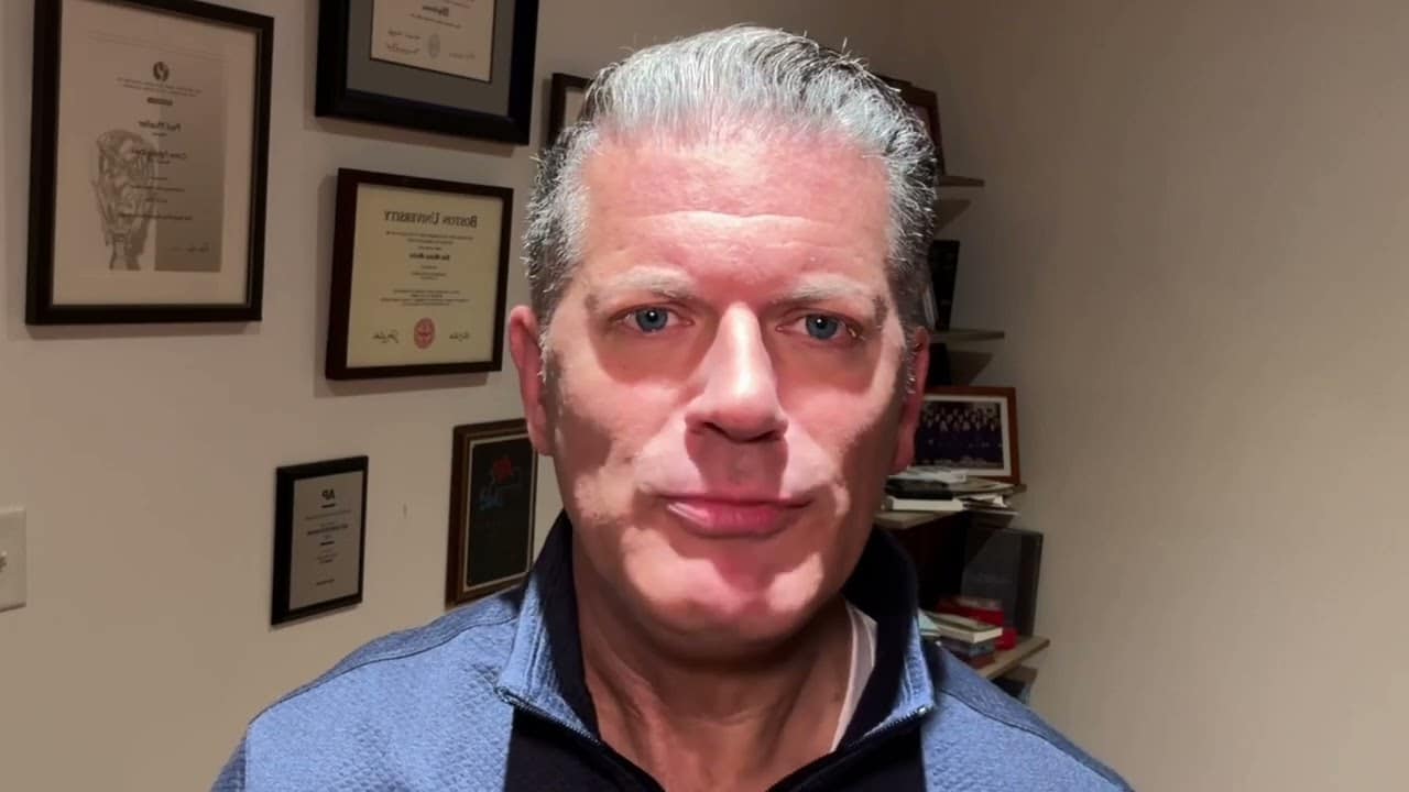 A man with grey hair and glasses in front of some pictures.