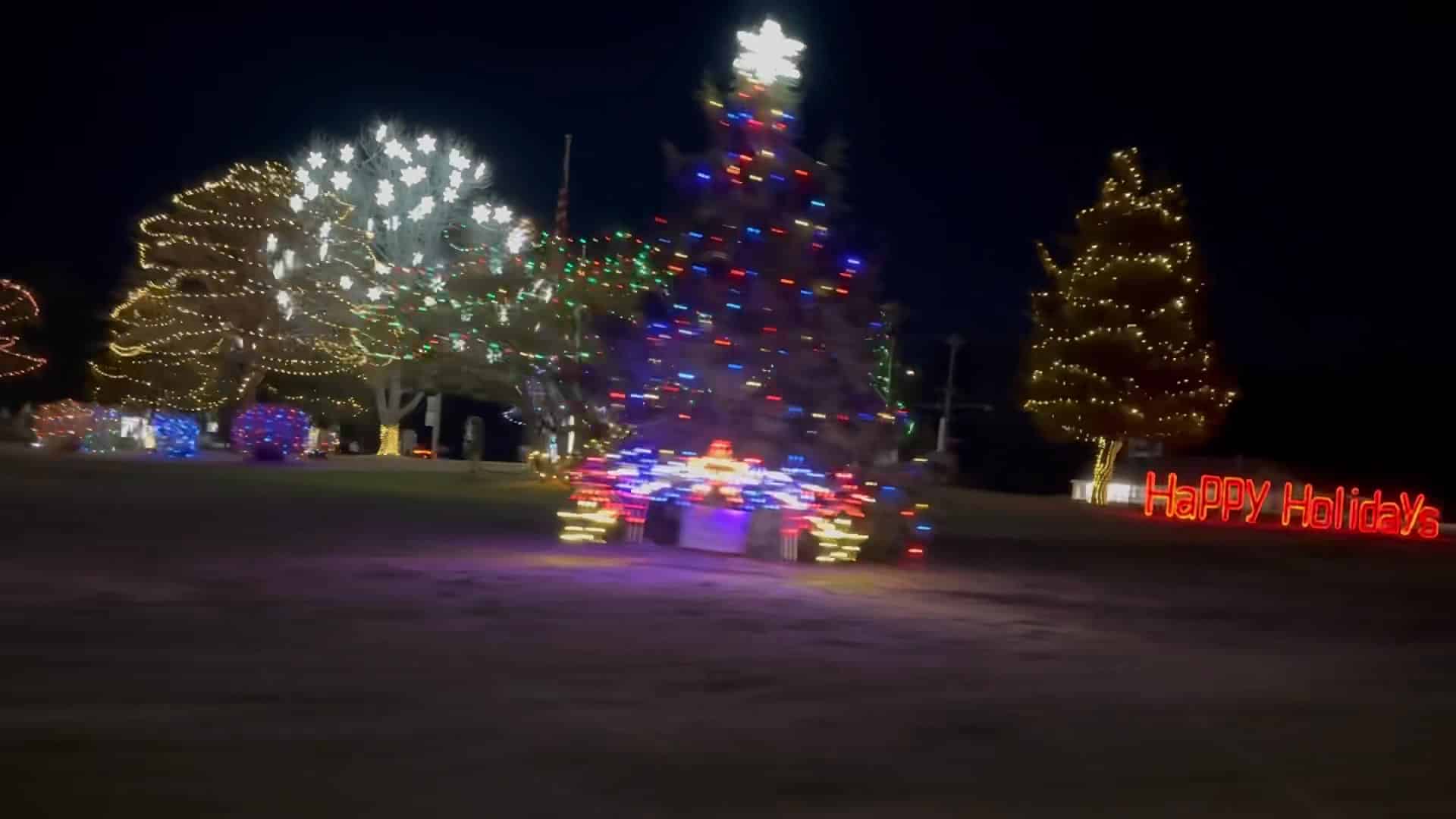 A car driving past a christmas tree at night.