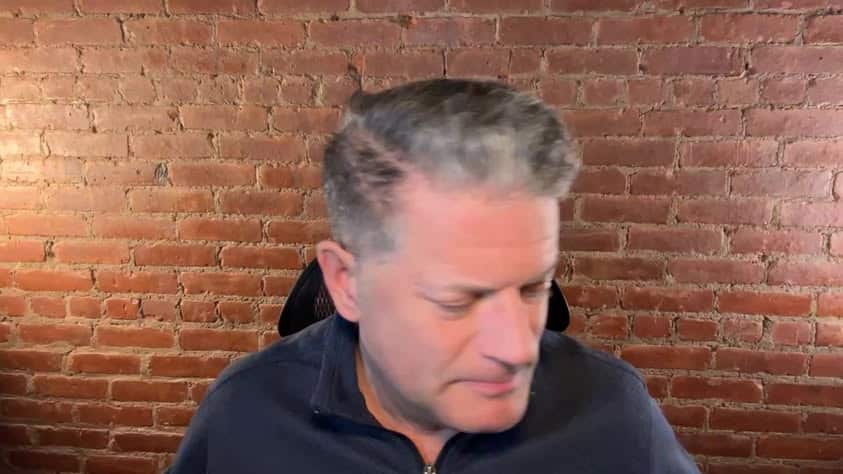 A man with gray hair sitting in front of a brick wall.