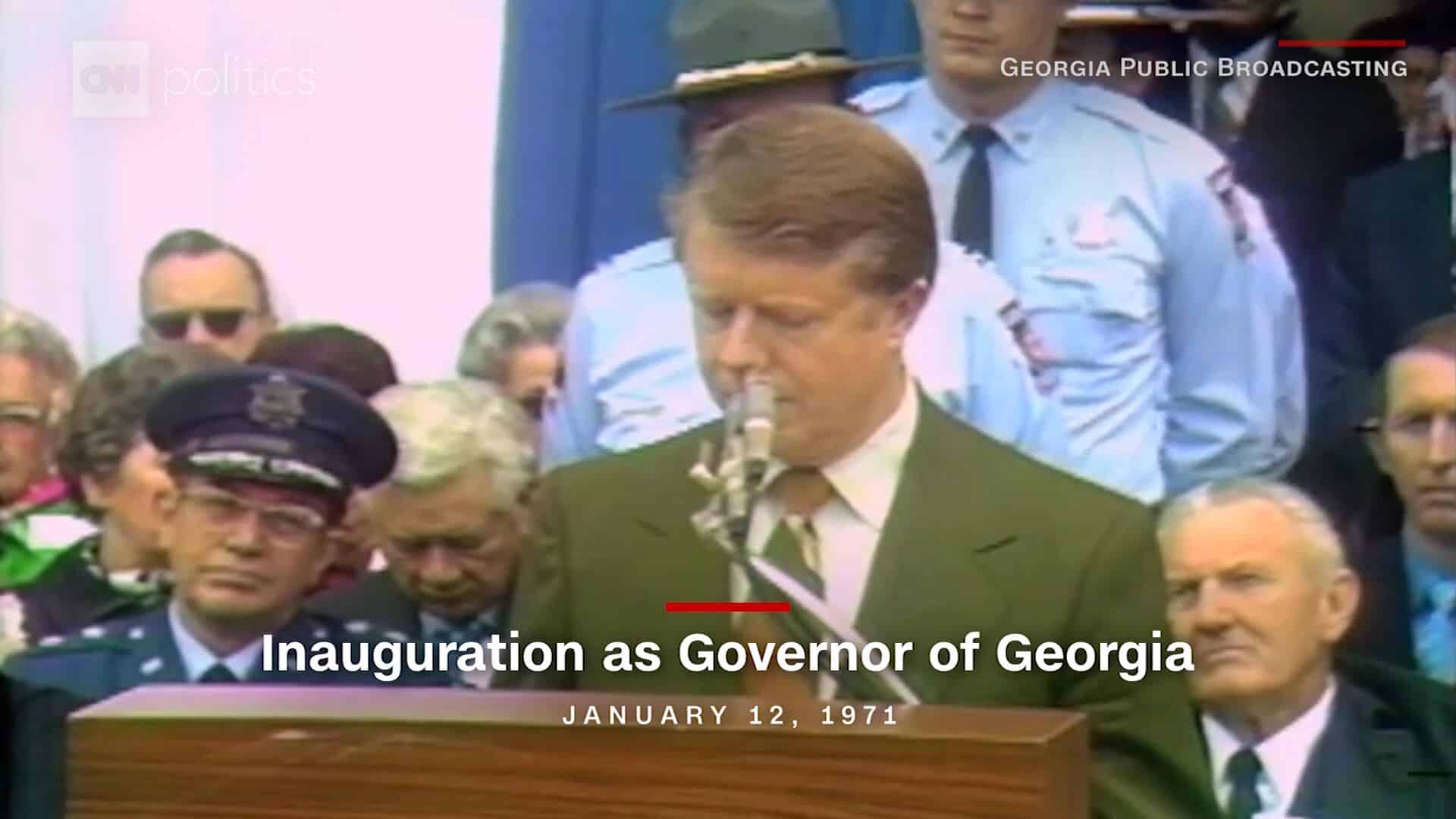A man in green jacket blowing into a pipe.