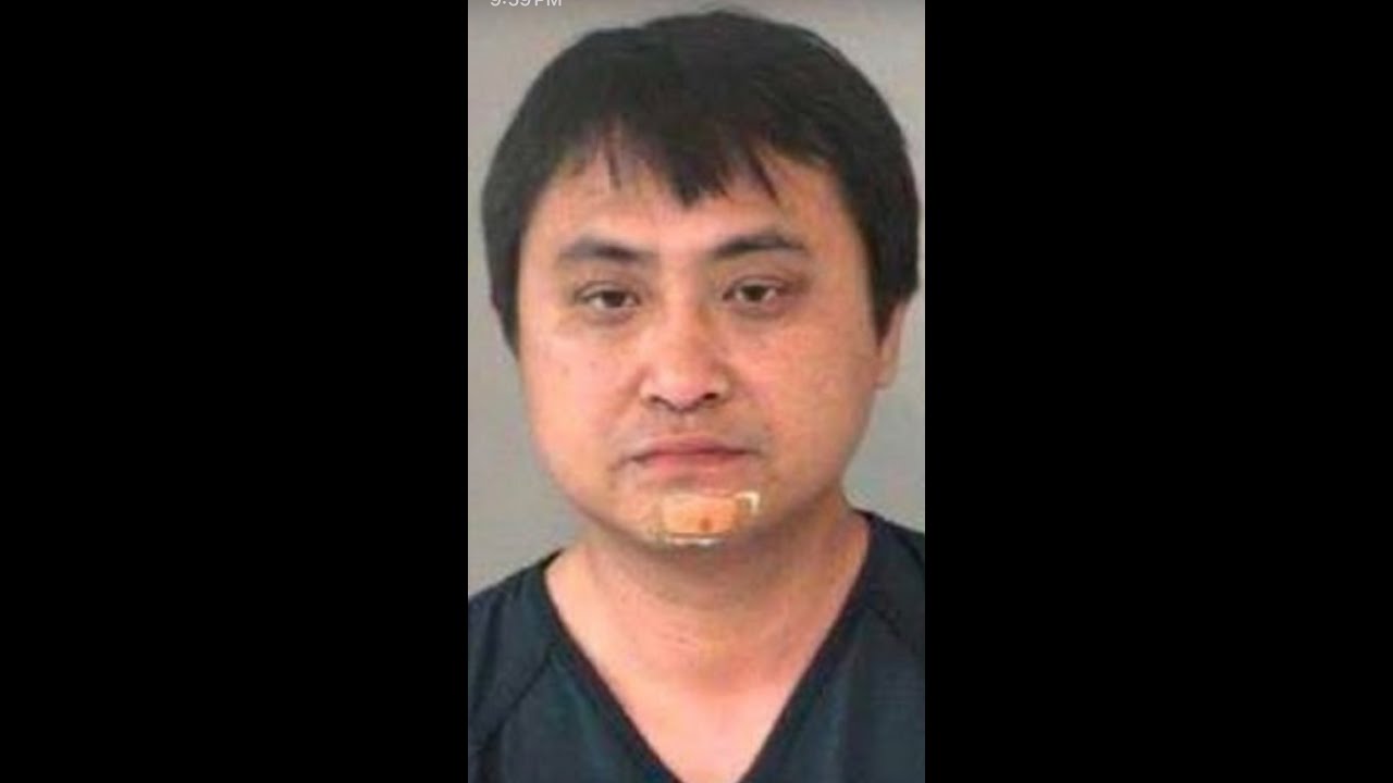 A man with black hair and glasses is in a police mug shot.