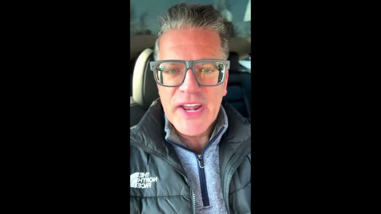 A man with glasses in the back of a car.