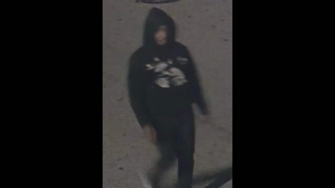 A man in black hoodie walking on sidewalk.